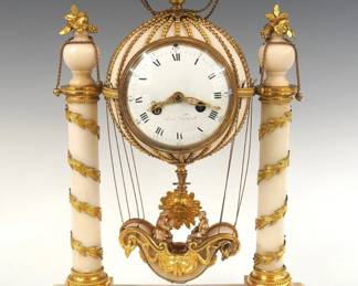 A late 18th century French Louis XVI Period Balloon form mantel clock by Henri Voisin, Paris.  8-day time and strike movement with silk thread suspension features a convex porcelain dial with Roman hour numerals within a ring of Arabic minute numerals, pierced Fleur-De-Lis hands and an Apollo mask pendulum bob.  The dial is marked "Henri Voisin", Voisin was a member of the Paris juré (the guild of master clockmakers) from 1773 to 1807.   White Marble case with gilded Bronze detail in the form of a hot air ballon, the balloon form movement housing with hanging passenger basket is supported by two turned columns with gilded foliate decoration on a shaped base with foliate panels and gilded cast detail.  Minor wear and small losses to the case, the passenger figures appear to be old replacements, lacks glass in rear door, movement with older repairs runs momentarily.  ESTIMATE $4,000-6,000