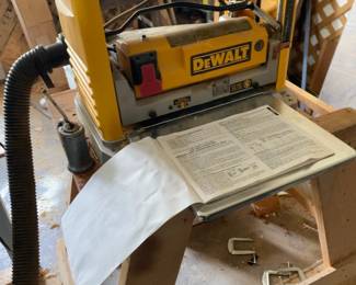 DeWalt benchtop thickness planer with dust-collection hose and stand. Heavy-duty woodworking machine for smoothing boards and producing consistent lumber thickness.