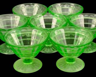 384 - 7 Uranium Green Glass Footed Sherbets (Description): Each piece measures 3 inches by 3.25 inches.  The glasses display the characteristic green  glow associated with uranium glass and  feature a footed pedestal design with ribbed  detailing.