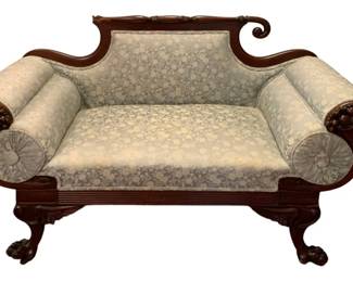 702 - American Empire Style Carved Mahogany Sofa (Description): Antique sofa featuring carved wooden frame  with scrolled arms and claw feet. Upholstered  in a light-colored floral patterned fabric  with bolster pillows at each arm. Measures 31  inches high by 52.5 inches wide by 23.5 inches deep.