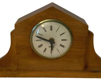 228 - West Germany Mantle Clock 6"x10.5"x2" (Description): West Germany mantle clock featuring a wooden  case with a peaked top design. The clock has  a round face with Roman numerals and a  brass-toned bezel. Measures 6 inches high by  10.5 inches wide by 2 inches deep. Used as is electric/electronic/mechanical  item. No guarantee all components, untested.