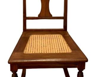 691 - Antique Rocker 32"x17"x28.5" (Description): Antique chair rocker featuring a traditional  design with a cane seat and turned front  legs. The chair has a vase-shaped splat in  the backrest. Measures 32 inches high by 17  inches wide by 28.5 inches deep.