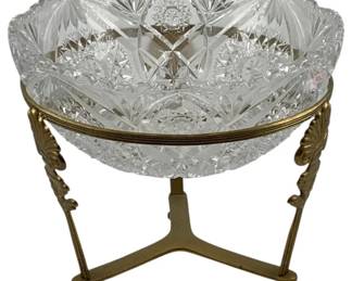 224 - Cut Glass Bowl w/ Brass Stand 8.5"x10" (Description): Cut glass bowl with brass stand. The bowl  features intricate cut glass patterns and  rests on an ornate brass stand with  decorative shell motifs and tripod legs.  Measures 8.5" x 10".