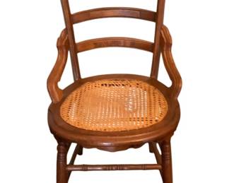 150 - Antique Chair 34.5"x19"x19" (Description): Antique chair featuring a ladder back design  with curved arms and a cane seat. The chair  has turned legs with stretchers. Measures  34.5 inches tall by 19 inches wide by 19  inches.
