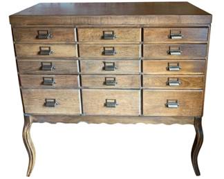 667 - Antique 15-Drawer Oak Filing Cabinet (Description): A 15-drawer cabinet featuring multiple small  storage compartments with metal label holder  pulls. The piece rests on cabriole legs with  a scalloped apron. 32.5"x11.25"x16"
