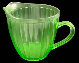 371 - Uranium Green Glass Pitcher 5.5"x7.25"x5" (Description): Uranium glass pitcher featuring a ribbed  design with applied handle. The pitcher is  chipped. Measures 5.5 inches by 7.25 inches  by 5 inches.