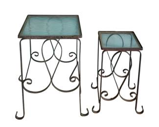 7 - Nesting Tables w/ Glass Tops (Description): Two-piece set of nesting tables featuring  decorative wrought iron bases with scrollwork  design and glass tops. Sold as is with  cracked glass. Larger table measures 20" x  12.5" x 12.5".