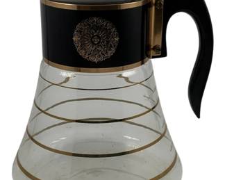 497 - Mid-Century Coffee Carafe 8"x6.5" (Description): Mid-Century coffee pot featuring a clear  glass carafe with gold stripe detailing and a  black collar with decorative gold medallion.  The pot has a black handle and hinged lid.  Measures 8 inches by 6.5 inches.