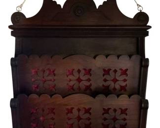 164 - Wood Wall Pocket Shelf 27"x24"x6" (Description): A decorative wood wall pocket shelf featuring  carved scalloped edges and ornate cutwork  designs. The piece has a shaped crest at the  top with circular medallion accents and two  tiered pocket sections for display or storage. Measures 27 inches wide by 24 inches  tall by 6 inches deep.