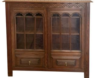 106 - Antique Cabinet Bookcase 48"x50"x12" (Description): Antique cabinet bookcase featuring  Gothic-inspired arched glass panel doors with  carved detailing along the frieze. The piece  includes two lower drawers with brass drop  pulls. Constructed of oak with interior shelving for display or book storage.  Measures 48 inches wide by 50 inches tall by  12 inches deep.