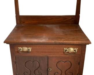 600 - Antique Washstand w/ towel bar 47"x28"x16" (Description): Antique washstand featuring carved cabinet  doors, brass drawer pulls, and a towel bar.  Measures 47 inches high by 28 inches wide by  16 inches deep.