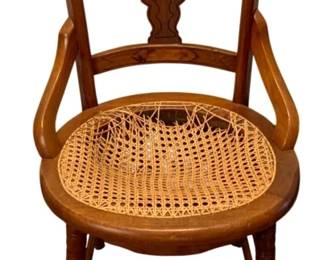 690 - Antique Chair 33.5"x17.5"x17" - as is (Description): Antique chair featuring a carved wooden frame  with decorative back splat, curved arms, and  a cane seat. The chair stands on turned legs  with stretcher supports. Measures 33.5  inches high by 17.5 inches wide by 17 inches deep.