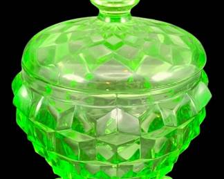 323 - Fostoria Cubist Sugar Dish Uranium Green Glass (Description): Fostoria "Cubist" pattern sugar dish crafted  in uranium glass. The piece features the  distinctive geometric cubist design with a  fitted lid topped by a decorative finial,  resting on ball feet. Measures 4" x 4".