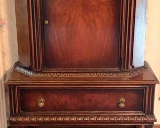 713 - Antique Cabinet in the Jacobean Revival Style (Description): 64.5"x40"x17" - Antique cabinet in a server  style featuring rich wood construction with  decorative carved details. The piece includes  an upper cabinet section with a single door  and a lower section with a drawer, supported by turned legs with a carved stretcher base.  inches deep.