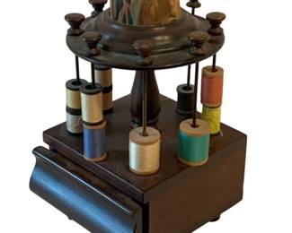650 - Antique Spool Holder 8"x4"x4.5" (Description): Antique spool holder featuring a turned  wooden stand with multiple spindles for  holding thread spools and a fabric-covered  pin cushion top. The base includes a drawer  for storage. Measures 8 inches by 4 inches by 4.5 inches.