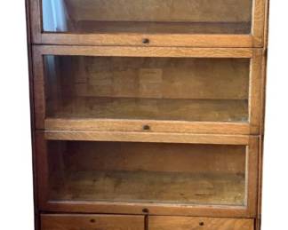 127 - Glass-Front Bookcase 55"x34"x12.5" (Description): Glass-front bookcase featuring three display  sections with lift-up glass panel doors and  two storage drawers at the base with metal  bail pulls. Measures 55 inches high by 34  inches wide by 12.5 inches deep.