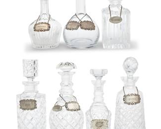 19 A group of seven cut glass decanters and five sterling silver tags Mid-20th century Five tags with British hallmarks for sterling, London, 1966, and maker: R & K; two metal alloy marked MADE IN ENGLAND; two marked: EMPIRE PEWTER; glass unmarked Comprising seven glass decanters of various styles and shapes, each with stopper, and five sterling silver tags, together with four non-silver tags, each labeled for a different spirit 17 pieces Tallest height 12 in., diameter 4 1/2 in.; shortest height 8 3/4 in., diameter 4 7/8 in. Total sterling weight 2.1 oz. troy approximately Estimate: $300 - $500