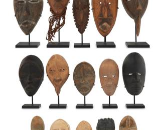 165 A group of West African carved wood dan masks 20th century The 'passport' masks, one mounted with cowrie shells and fibrous material, each raised on an enameled metal or acrylic stand 15 pieces Tallest height 6 1/2 in., width 2 3/4 in., depth 2 3/4 in. Estimate: $700 - $900