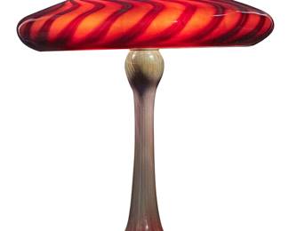 60 Joe Clearman (b. 1946) An art glass lamp, 1991 Base etched with signature, date, and number: J Clearman / 2499 / 2594 The glass base issuing three lights with brass heat cap, surmounted by a swirling glass shade, electrified Base height 24 in., diameter 8 7/8 in.; shade height 6 3/4 in., diameter 18 3/4 in. Estimate: $700 - $1,000