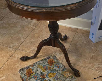 Lot 41: Round glass-top pedestal table with carved wooden base and floral upholstered ottoman