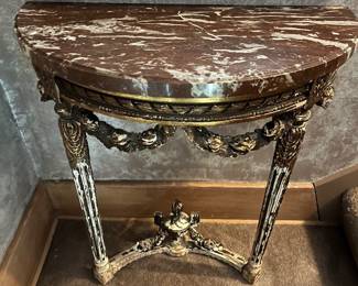 Antique French Louis XVI style demilune console table featuring a marble top and carved, gilded wood legs.