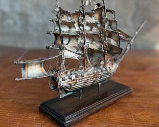 This lot features a sterling silver ship sculpture that sits on a wood plinth. The silver weight alone is 223.89 grams. This piece measures (with plinth), 8” H x 12” W x 3” D.