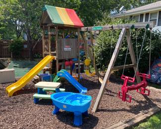 backyard wooden playset featuring a yellow wave slide, swings, and a multi-colored canopy