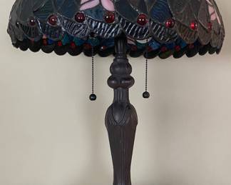 Tiffany-style table lamp features a stained glass shade decorated with blue and purple dragonfly patterns