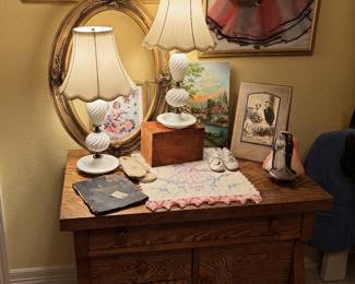 Antique dresser, lace, milk glass lamps and framed vintage children’s clothing