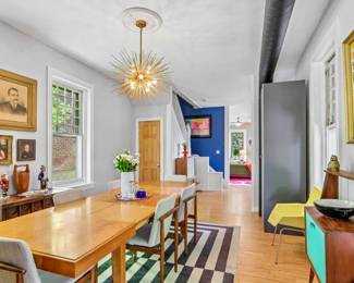 Walnut dining table with upholstered mid-century chairs, brass sputnik chandelier, secretary desk with teal accent, framed mounted butterfly specimen collection, antique portrait paintings, sideboard, black-and-white striped rug, brass frog and elephant figurines.