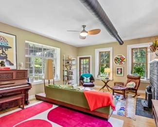 Vintage upright piano and bench, Toulouse-Lautrec exhibition poster, mid-century green tufted sofa, teak and leather lounge chairs, ladder bookshelf, red and pink graphic wool area rug.