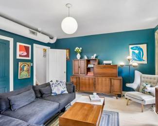 Wood plank coffee table, mid-century teak credenza with cane doors, tufted wingback chair with ottoman, framed Matisse-style print, blue velvet sofa, framed art collection.