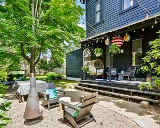 Backyard patio with metal chiminea, Adirondack chairs, wicker egg swing chair on porch, string lights and paper lanterns, wrought iron patio chairs, teak dining table, hanging planters.