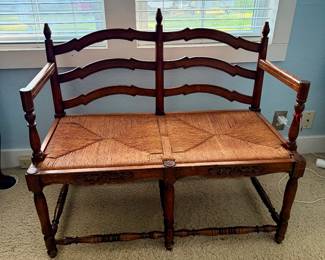 Charming French Provincial-style walnut bench featuring a beautifully hand-rushed seat, carved floral apron, turned legs, and classic ladder-back design.