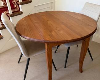 Round drop-leaf dining table in warm knotty pine with shaped cabriole legs, paired with three modern channel-tufted ivory linen chairs on slim black metal legs. $150 set.