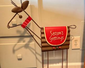 This is a rustic corrugated metal "Season's Greetings" rocking reindeer holiday tabletop figurine featuring a red saddle blanket and wire legs.