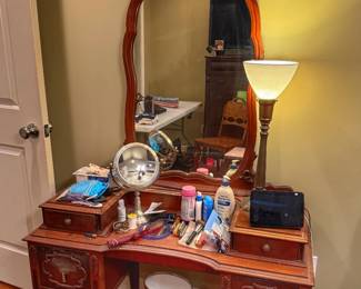 Vintage wooden vanity featuring an ornate arched mirror, multiple drawers, decorative carved scrollwork, and brass-toned hardware. This classic American traditional design, inspired by the Jacobean Revival style of the 1920s to 1940s.