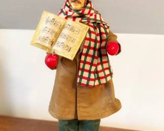 This is a vintage 1987 Clothtique Possible Dreams Christmas Caroler Man, identifiable by his signature stiffened-fabric costume, red and green plaid scarf, green Tyrolean-style hat, and open songbook.
