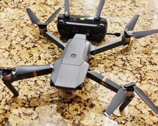 DJI Mavic Pro Drone Package DJI Mavic Pro foldable camera drone, Model M1P, complete with DJI remote controller and Lowepro padded carrying backpack. Package includes multiple DJI Intelligent Flight batteries, battery charging equipment, cables/power accessories, controller, and other accessories shown. Features a stabilized gimbal-mounted camera, GPS-assisted flight, compact folding design, and app-based flight controls.