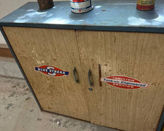 Lot 24: Two-door cabinet with ignition decals, lubricant cans, and spark plug boxes