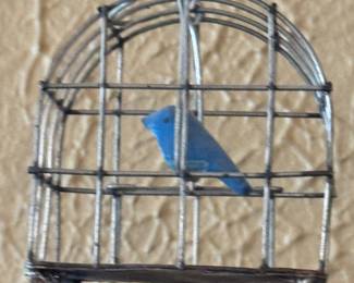 charming decorative tabletop figurine features a vibrant blue bird figurine enclosed inside a rustic, arched wire-mesh cage