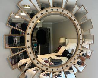 Modern, round sunburst wall mirror featuring a gold metal frame and numerous smaller, angled mirrors surrounding the center.