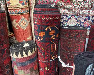 Collection of rolled tribal and traditional rugs in rich red and earth tones