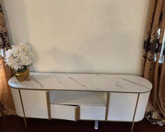 Modern White & Gold TV Stand / Media Console Description: Beautiful modern TV console with fluted cabinet doors, white marble-look top, and gold accents. Perfect as a TV stand, media console, or storage cabinet. Features: * White finish with fluted doors * Marble-look top * Gold hardware and legs * Open center shelf for media devices * Two storage cabinets and two drawers Good condition. Smoke-free home.