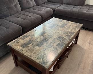 Large rectangular lift-top coffee table with a brown stone/marble-look top and dark wood base. The tabletop lifts up and toward you, creating a raised surface that’s great for eating or working from the sofa, with hidden storage underneath. Also features a lower storage shelf and drawer.