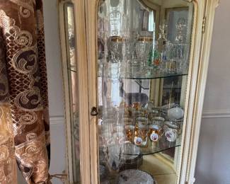 Elegant Curio / China Cabinet – Ornate Cream Finish Description: Beautiful cream-colored china cabinet with glass doors, mirrored back, glass shelves, and ornate detailing. Perfect for displaying china, crystal, collectibles, or home décor. Features: * Mirrored interior * Glass shelves * Elegant carved details * Cream finish with subtle gold accents. Light included inside ceiling up top.