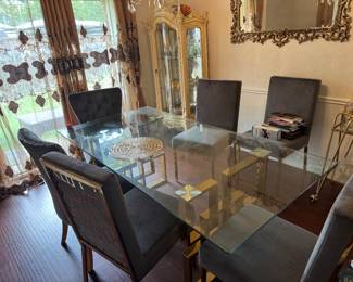 Modern Glass Dining Table with 6 Chairs – Gold Base Beautiful contemporary dining set featuring a thick tempered glass tabletop with a gold geometric metal base and six upholstered gray dining chairs. Great condition and perfect for a modern dining room. * Seats 6 comfortably * Glass top * Gold metal base * Six upholstered chairs included