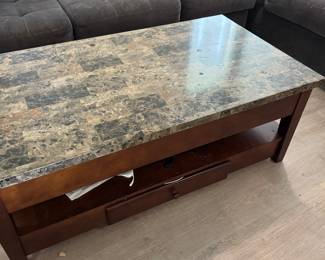 Large rectangular lift-top coffee table with a brown stone/marble-look top and dark wood base. The tabletop lifts up and toward you, creating a raised surface that’s great for eating or working from the sofa, with hidden storage underneath. Also features a lower storage shelf and drawer.