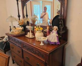 Beautiful traditional solid wood dresser with an attached mirror, accented by decorative lamps, porcelain figurines, and vintage home décor. Quality bedroom furniture and timeless furnishings available at this Tavares, Florida estate sale hosted by Kinfolk Estate Sales.
