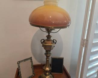 Vintage brass table lamp with a peach glass shade displayed alongside decorative accessories and framed artwork. Classic home décor and timeless furnishings available at this Tavares, Florida estate sale hosted by Kinfolk Estate Sales.